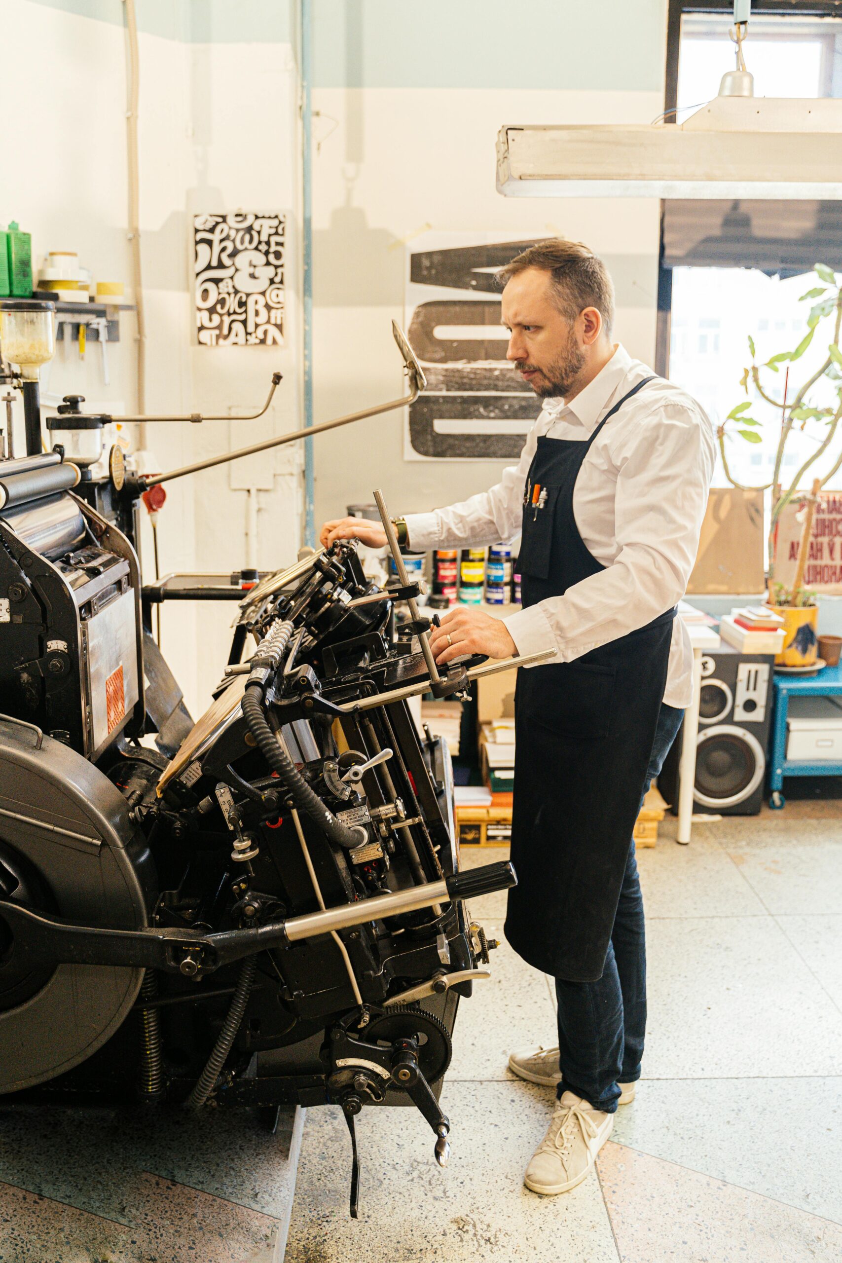 An adult male operates a vintage printing machine inside an industrial workshop setting.